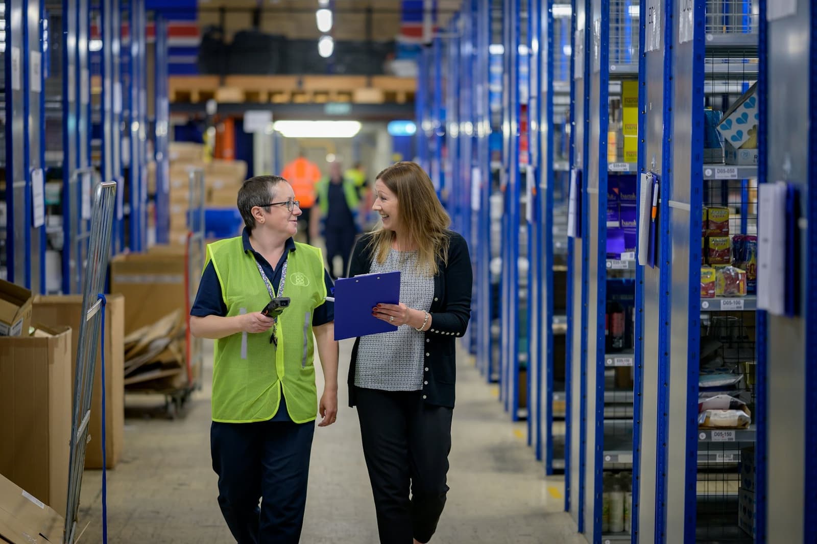 Two colleagues walking down a warehouse aisle lined with stocked shelves